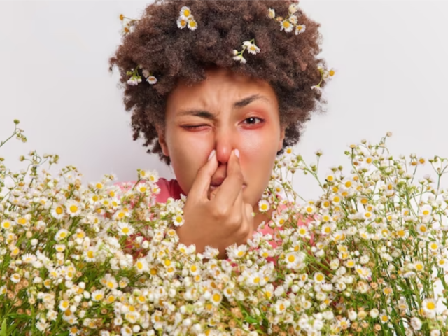 آلرژی با تصویر زنی با موی مجعد پشت گل های متنوع که حساسیت داره و بینی خور رو گرفته