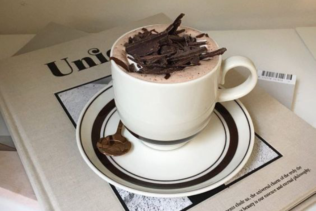 هات چاکلت در ظرف سفید با تزیین شکلات که روی یک کتاب است.